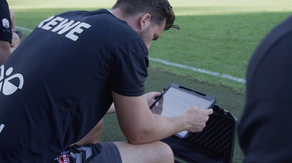 Um treinador de futebol usando um tablet com software de análise de desempenho durante uma sessão de treinamento.