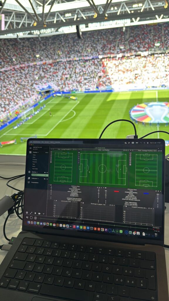 A laptop displaying the Catapult MatchTracker interface during a live football match at a packed stadium.